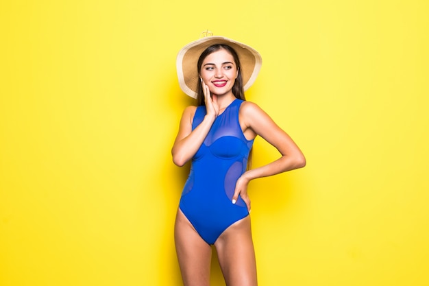 Attractive girl in a white bikini, hat, sunglasses, emotionally opened mouth on a yellow wall with a perfect body. Isolated. 