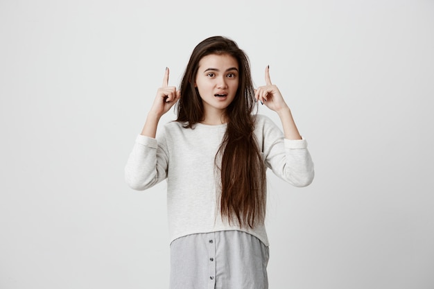 attractive good-looking excited woman with black long hair pointing fingers up having surprised look, with cheerful and happy expression of face