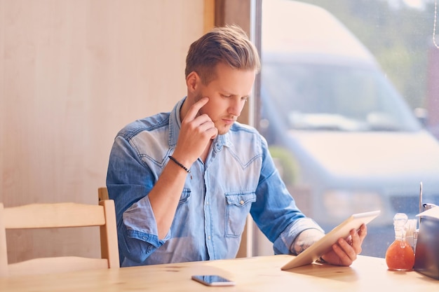 Attractive guy using a tablet PC in a cafe near the window.