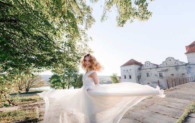 Free Photo attractive happy blonde girl dressed in white dress is turning around and smiling on the sunny day near old stone castle