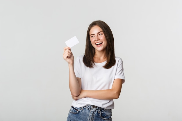 Attractive happy brunette girl laughing and holding credit card, white.