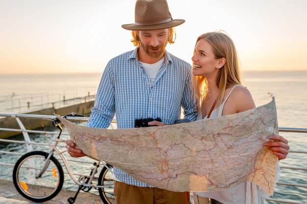 Free photo attractive happy couple traveling in summer on bicycles, man and woman with blond hair boho hipster style fashion having fun together, looking in map sightseeing