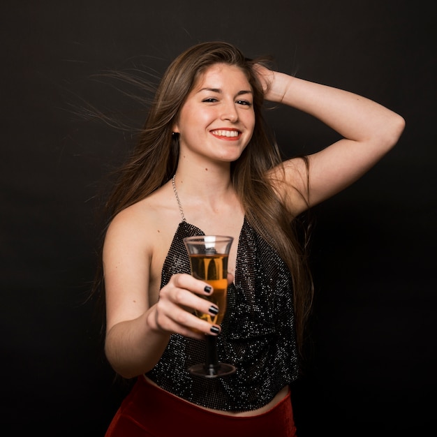 Attractive happy lady in evening cloth with glass of drink and hand on head 