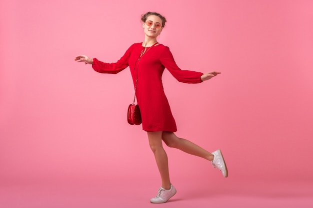 Attractive happy smiling stylish woman in red trendy dress jumping running on pink wall isolated, spring summer fashion trend, romantic mood flirty girl