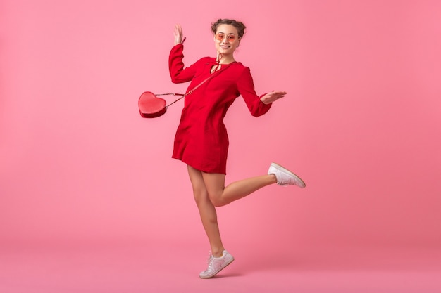 Attractive happy smiling stylish woman in red trendy dress jumping running on pink wall isolated, spring summer fashion trend, romantic mood flirty girl