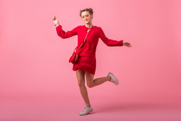 Attractive happy smiling stylish woman in red trendy dress jumping running on pink wall isolated, spring summer fashion trend, romantic mood flirty girl