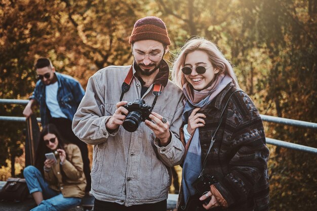 Free photo attractive hipster is showing photos for her smiling girlfriend at autumn park.