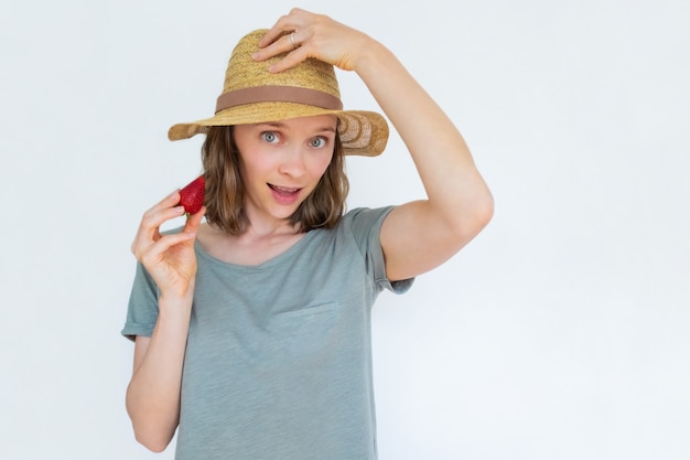 Attractive lady in hat holding ripe strawberry and greeting