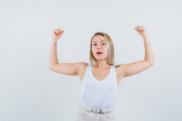 Attractive lady raising her arms showing her muscles in white blouse and looking self-confident