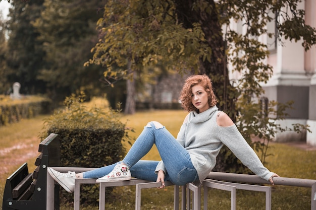 Free photo attractive lady in street wear sitting and putting legs on rail