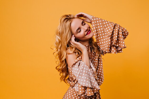 Attractive long-haired girl in brown dress posing  Amazing curly female model dancing in yellow wall.