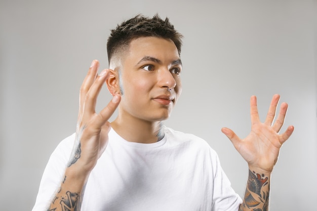 Attractive male half-length front portrait on gray studio backgroud. Young emotional surprised man.