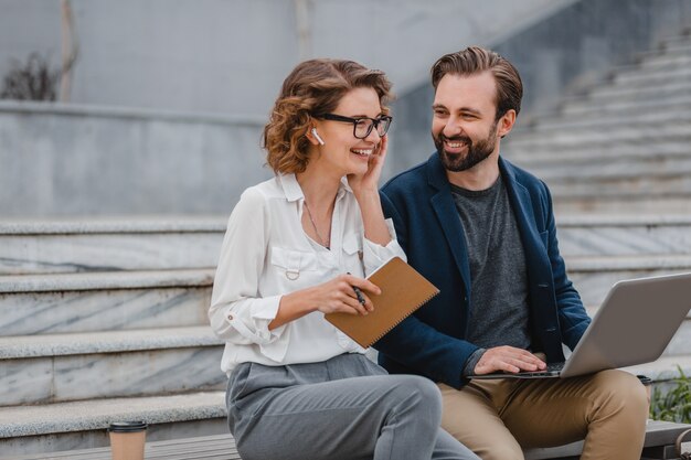 Attractive man and woman sitting on stairs in urban city center, working together on laptop