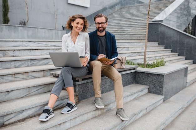 Free photo attractive man and woman sitting on stairs in urban city center