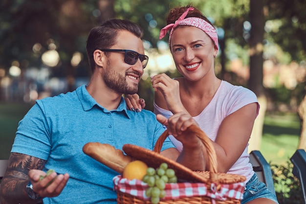 Attractive middle age couple during dating, enjoying a picnic on a bench in the city park.