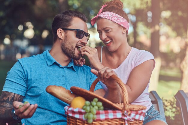 Attractive middle age couple during dating, enjoying a picnic on a bench in the city park.