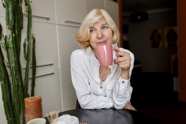 Free Photo attractive middle-aged blonde woman relaxing at home on the kitchen and drinking coffee