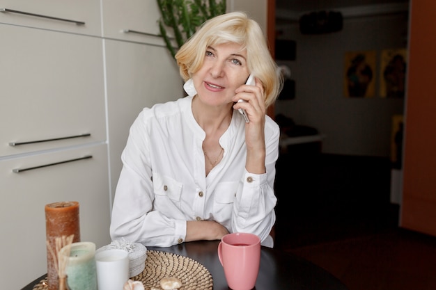 Free Photo attractive middle-aged blonde woman relaxing at home on the kitchen and talking by mobile phone