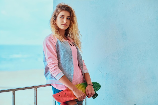 Free photo attractive pensive girl is posing for photographer with skateboard near seaside.