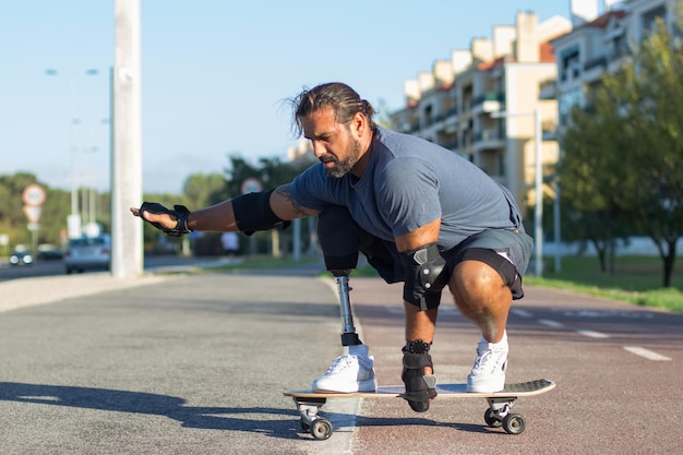 Free photo attractive person with disability doing sports in park. mid adult sportsman skateboarding down special road in concentration. sport, disability, training concept