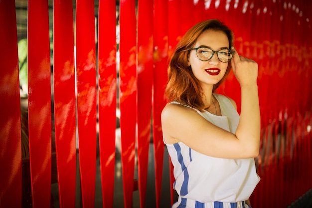 Attractive redhaired woman in eyeglasses posing against red background