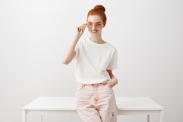 Free photo attractive redhead girl in sunglasses leaning on table and smiling