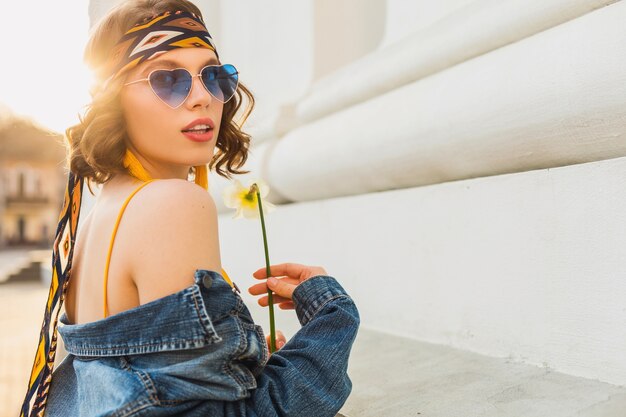 Attractive sexy stylish woman in yellow stylish dress wearing denim jacket, trendy outfit, spring summer fashion trend, sunny, blue sunglasses, street fashion, hippie style, fashionable accessories