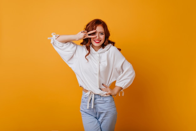 Attractive slim girl in oversize sweater expressing happiness. Good-humoured ginger woman dancing on yellow wall.