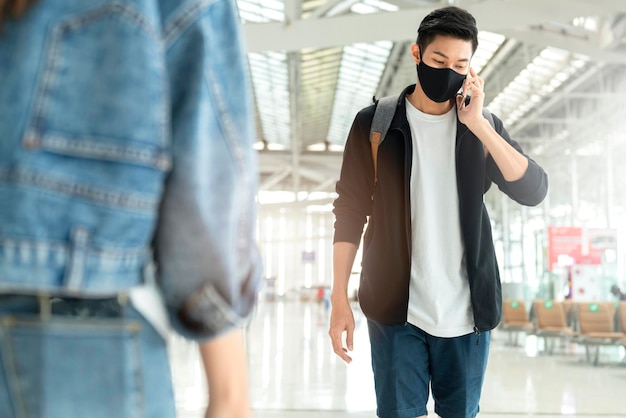 Free photo attractive smart asian male treveller casual cloth wear black protective face mask walking and hand use smartphone communication in airport terminal