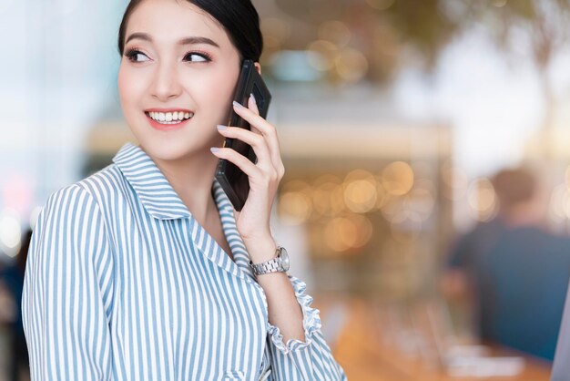 Attractive smart beautiful asian female well dress communication smartphone with cheerful and confident blur public space background