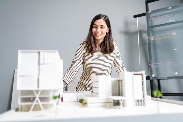 Attractive smiling engineer looking at architectural model in workplace