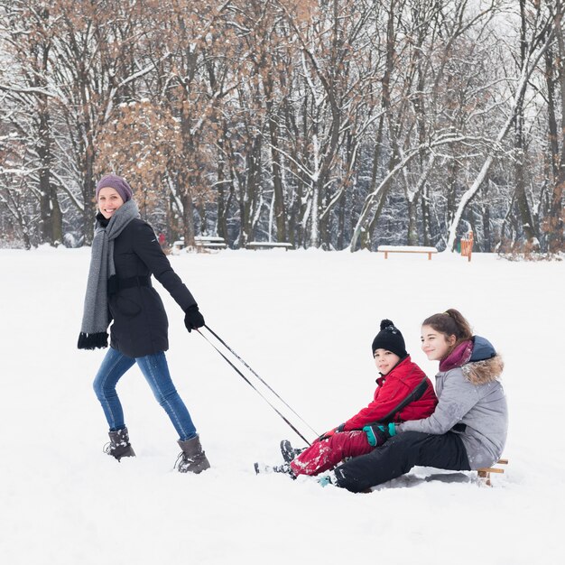 Attractive smiling mother pulling her children on sledge in winter