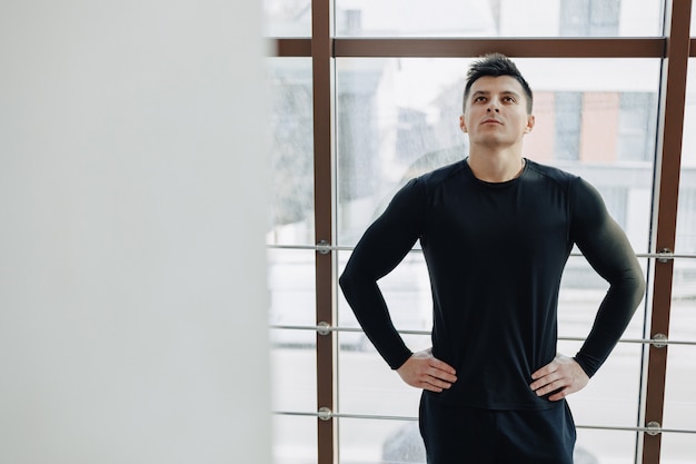 Attractive sporty guy by the window. athlete posing near spacious windows. gym and sports.