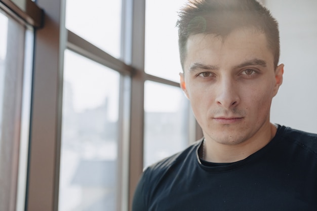 Attractive sporty guy by the window. athlete posing near spacious windows. gym and sports.