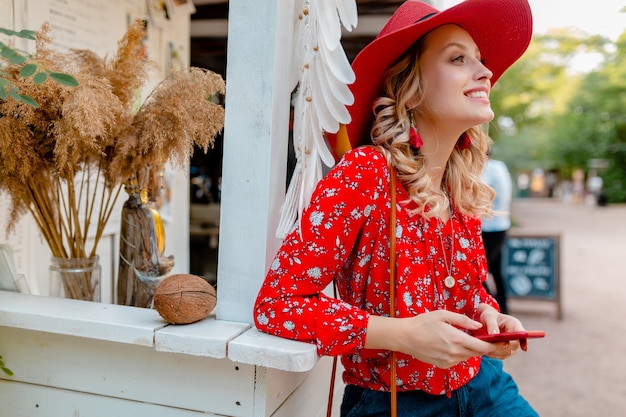 Free Photo attractive stylish blond smiling woman in straw red hat and blouse summer fashion outfit holding using smart phone  cafe