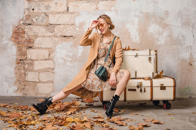 Free photo attractive stylish blonde woman in beige coat walking in street against vintage wall