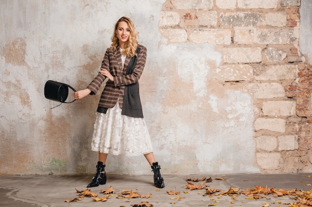 Free photo attractive stylish blonde woman in checkered jacket walking against wall in street