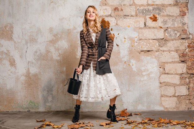 Attractive stylish blonde woman in checkered jacket walking against wall in street