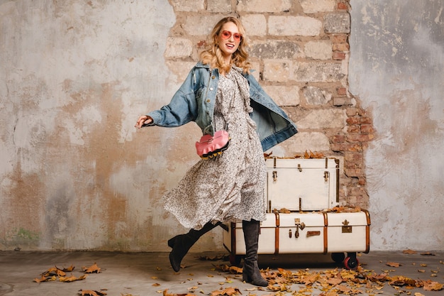 Free photo attractive stylish blonde woman in jeans and oversize jacket walking against wall in street