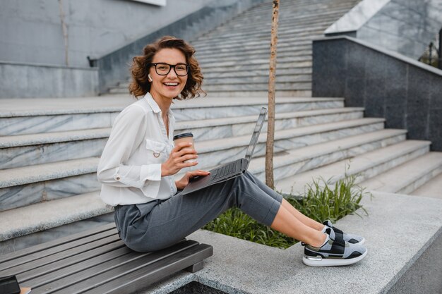 Attractive stylish smiling woman in glasses working typing on laptop