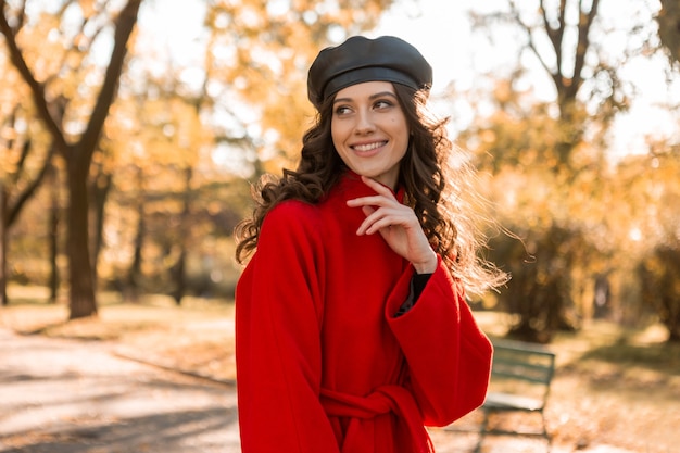 Free photo attractive stylish smiling woman with curly hair walking in park dressed in warm red coat autumn trendy fashion, street style, wearing beret hat