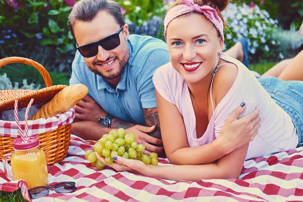 Attractive tattooed, bearded male and a redhead female lying on a blanket on a lawn in a park. Picnic time.