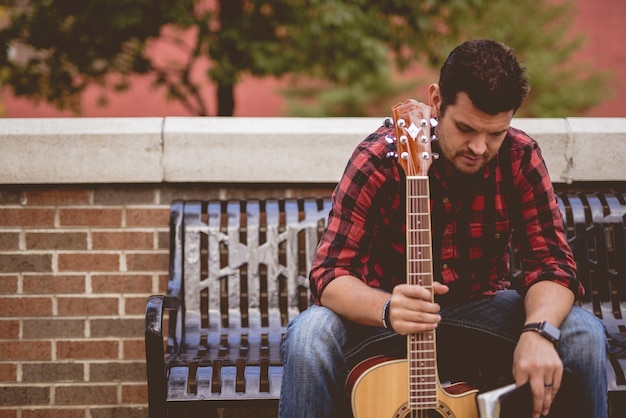 Free photo attractive white male sitting on a bench holding the guitar