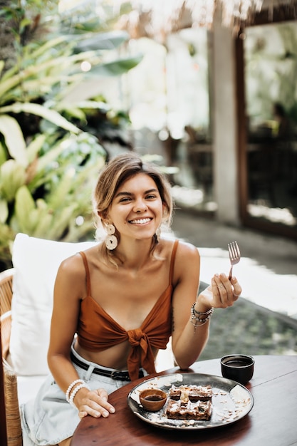 Free photo attractive woman in brown bra smiles widely and eats tasty waffle with ice cream and chocolate sauce