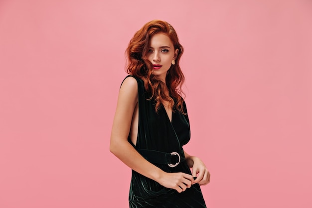 Attractive woman in dark dress looks at front on pink wall