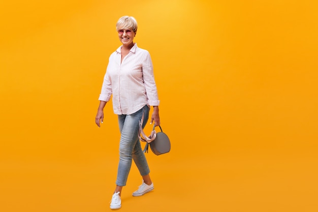 Free photo attractive woman in denim outfit moves on orange background and holds handbag