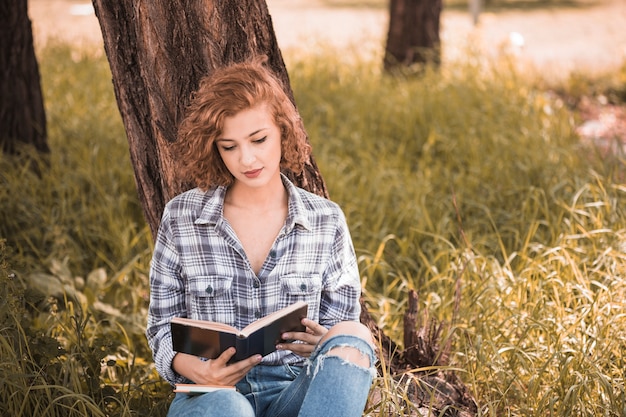 Free photo attractive woman leaning on tree and reading book