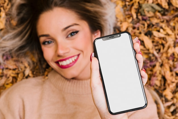 Free Photo attractive woman lying on dry leaves showing blank screen cellphone