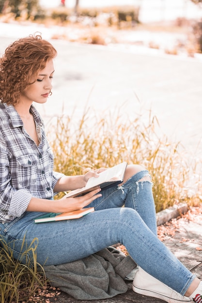 Free photo attractive woman sitting on grass and reading book