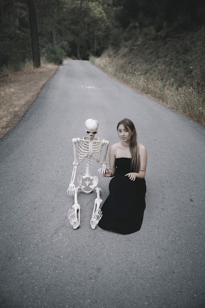 Free Photo attractive woman sitting on road with decorative skeleton of human and looking at camera